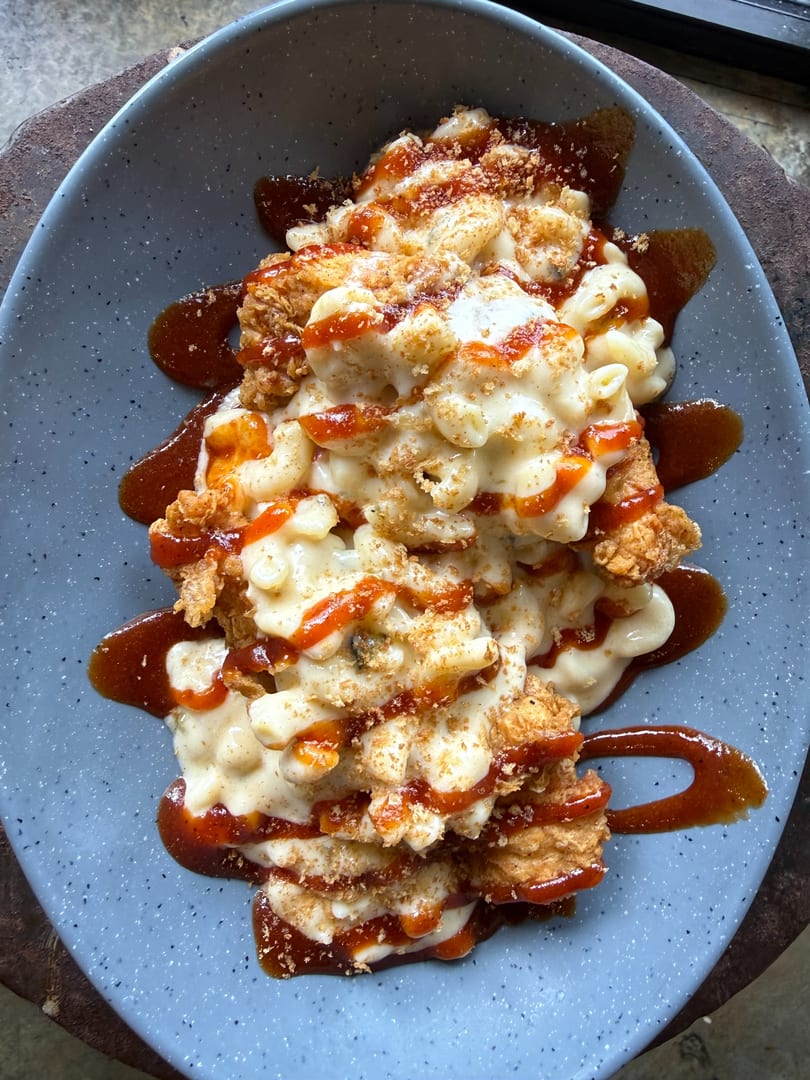Fried chicken and macaroni and cheese drizzled with hot sauce and barbecue sauce on a blue plate.