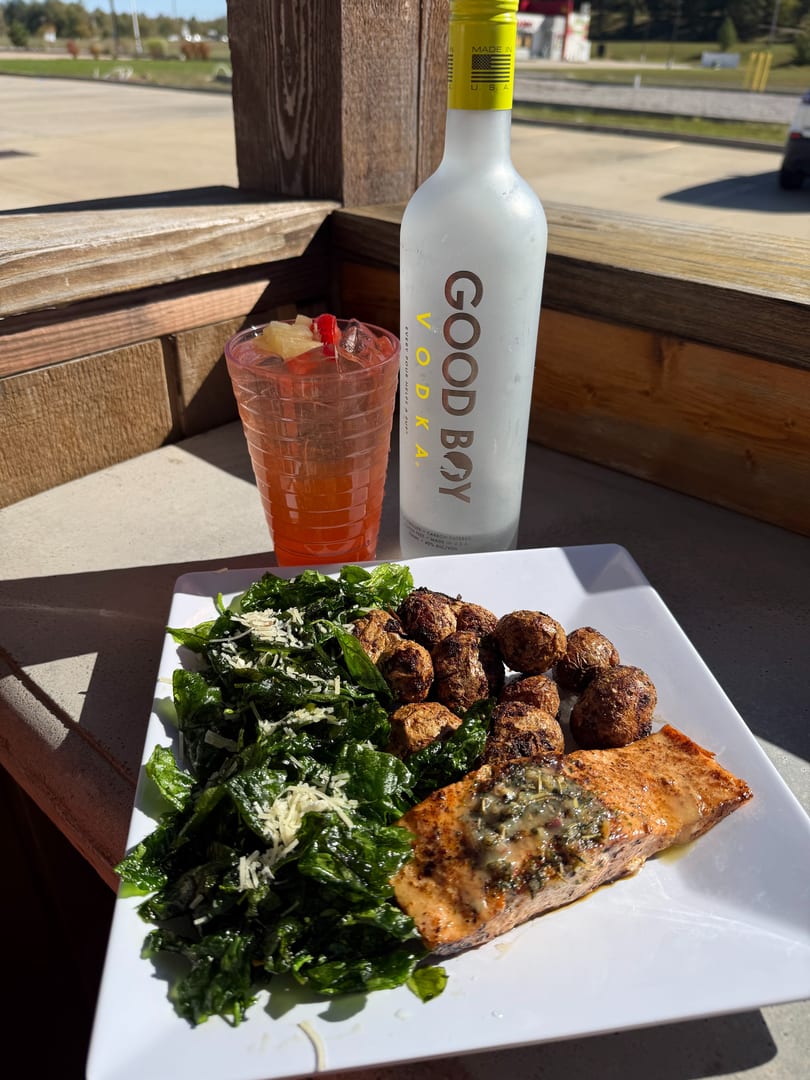Grilled salmon with roasted potatoes, spinach, and a cocktail next to a bottle of Good Boy Vodka.