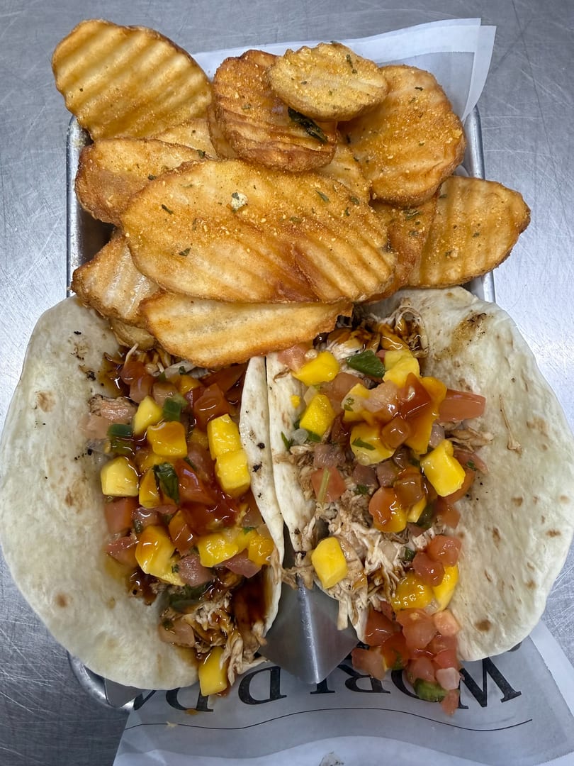 Two chicken tacos with mango salsa and waffle fries on a metal tray with paper liner.
