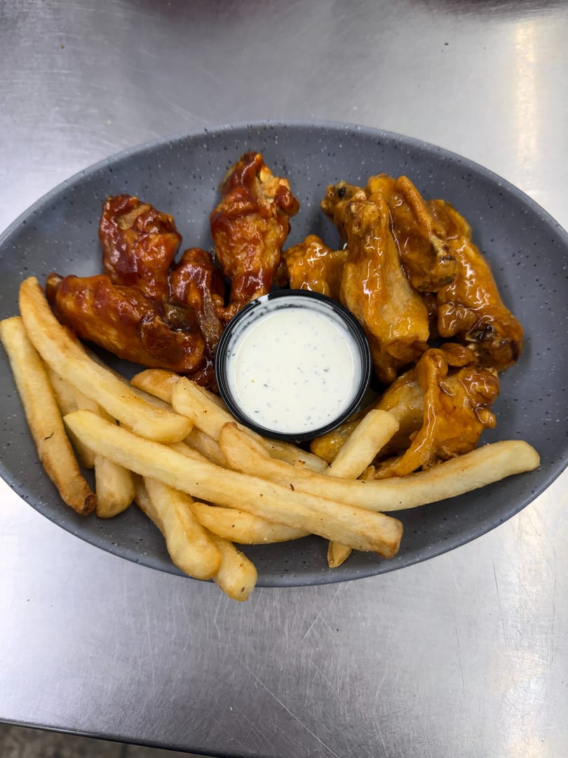 A gray plate holds two kinds of chicken wings, French fries, and a cup of ranch dressing.