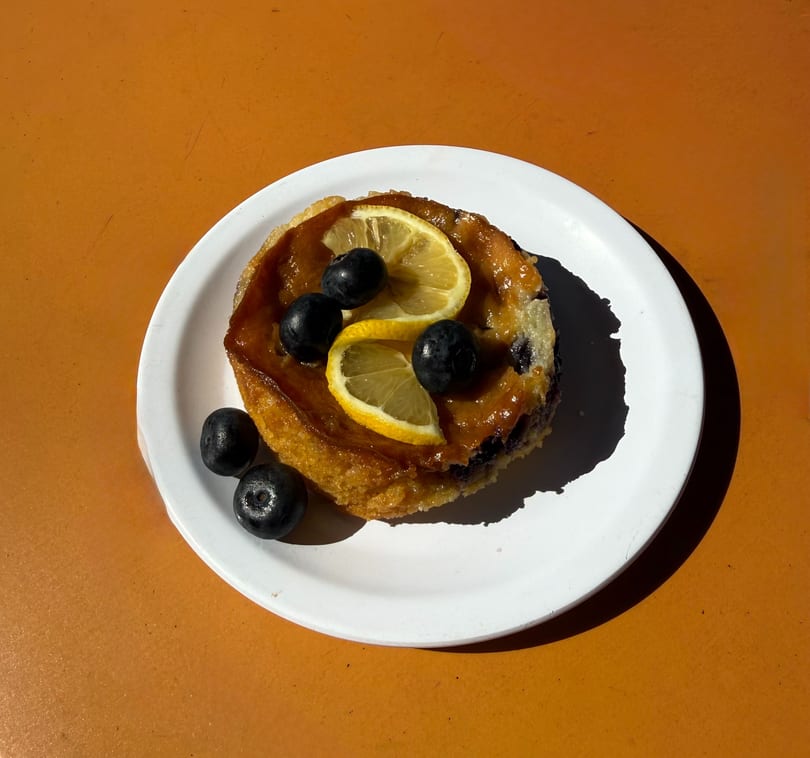 A golden-brown pastry topped with lemon slices and blueberries on a white plate.